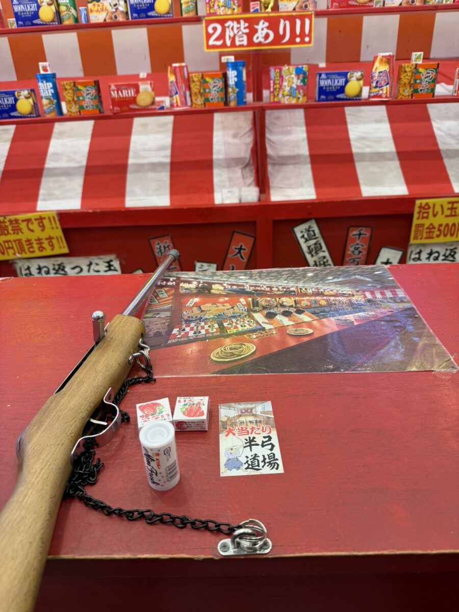 秘宝館本店の射的コーナー。木製の銃と景品のお菓子が台に並ぶ